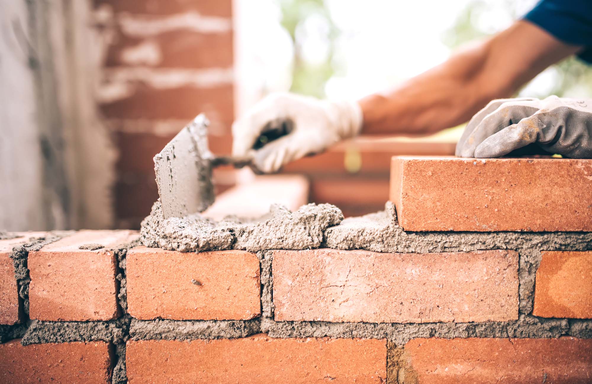 Bricklayer worker installing brick masonry on exterior wall with trowel putty knife and tools